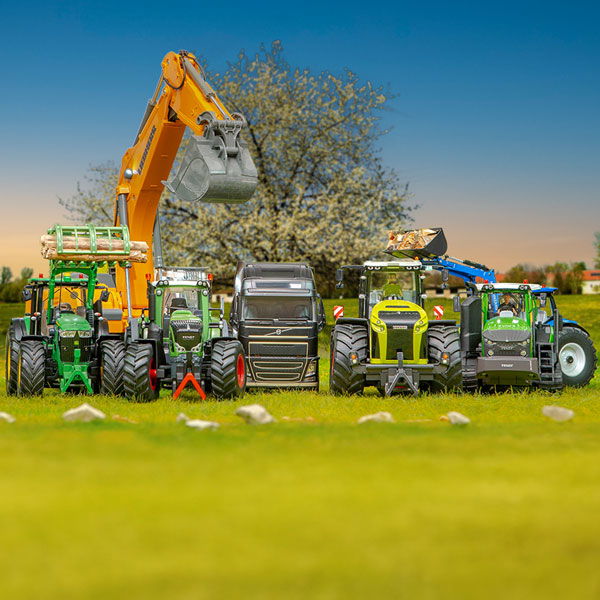 SIKCUONTROL Modelle von Bagger über LKW bis Traktoren stehen auf einer grünen Wiese mit Baum im Hintergrund. Der Himmel  zeigt einen schönen Sonnenuntergang.