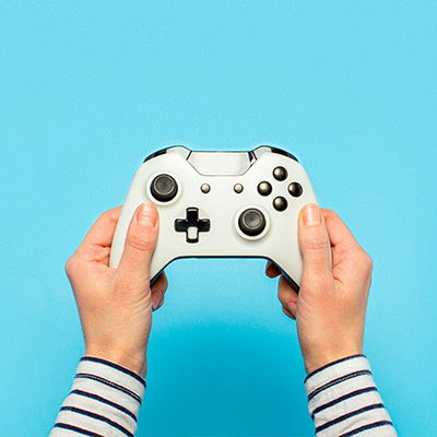 Zwei Frauenhände halten einen weißen Gaming-Controller. Der Hintergrund ist blau