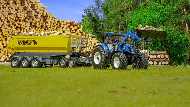 sikucontrol aktion mit anhänger ein sikucontrol new holland Traktor steht mit angehängtem Schmitz Cargobull 3-Achs-Kippsattelauflieger vor einem Wald und aufgestapeltem Holz